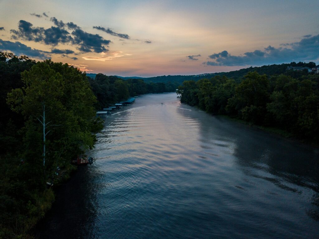 Aerial view of a serene river with lush trees at sunrise, capturing nature's tranquility in Hollister, Missouri.