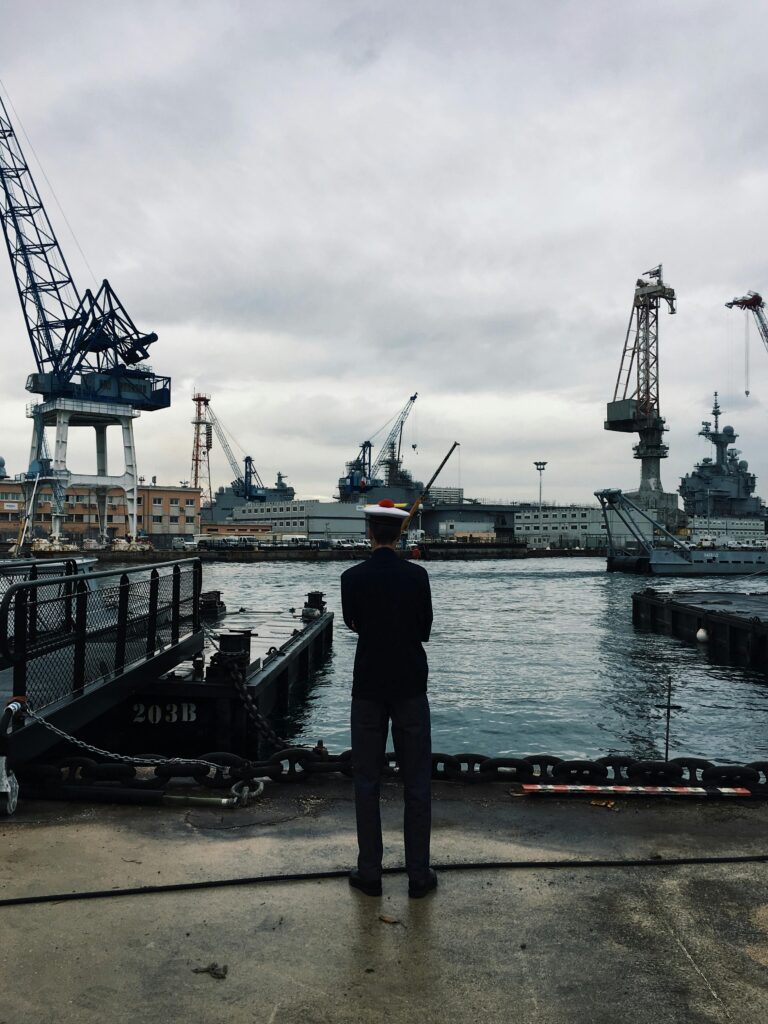 pexels-photo-2076828-2076828 Navy officer oversees ships at Toulon's industrial harbor under a cloudy sky.